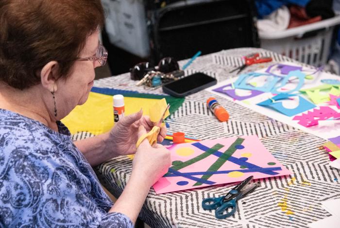 Person doing crafts with colorful paper, glue, and scissors on a patterned tablecloth.