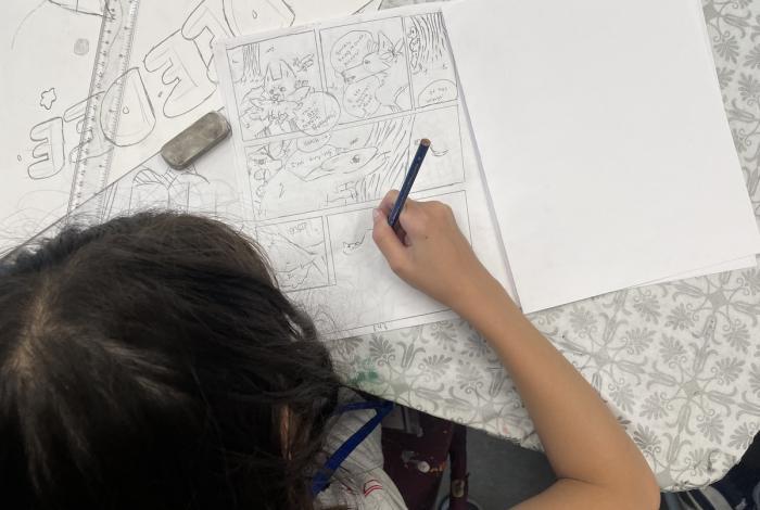 Person drawing a comic strip with a cat character on a paper.