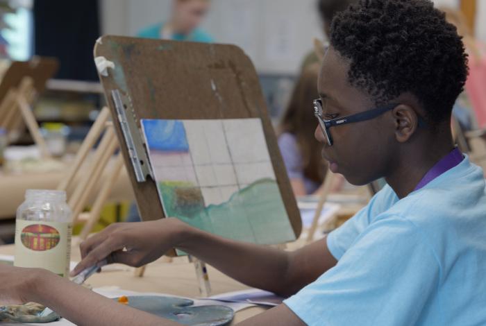 Person in a blue shirt painting on a canvas at an art class.